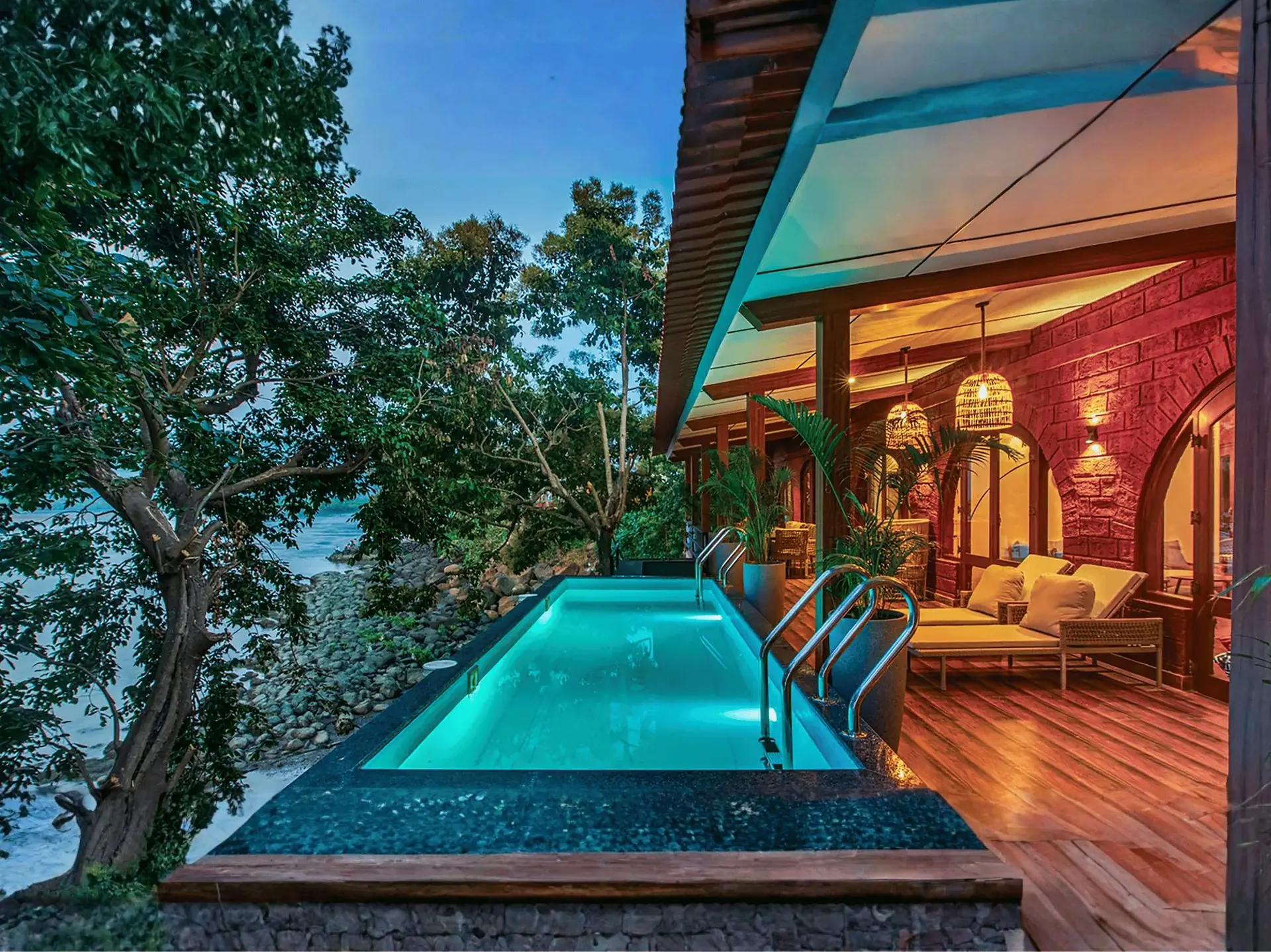 Lit infinity pool and timber deck of a beachfront Mulberry villa at dusk